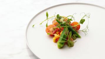 A white plate with a salad of tomatoes, greens, and yellow cubes.