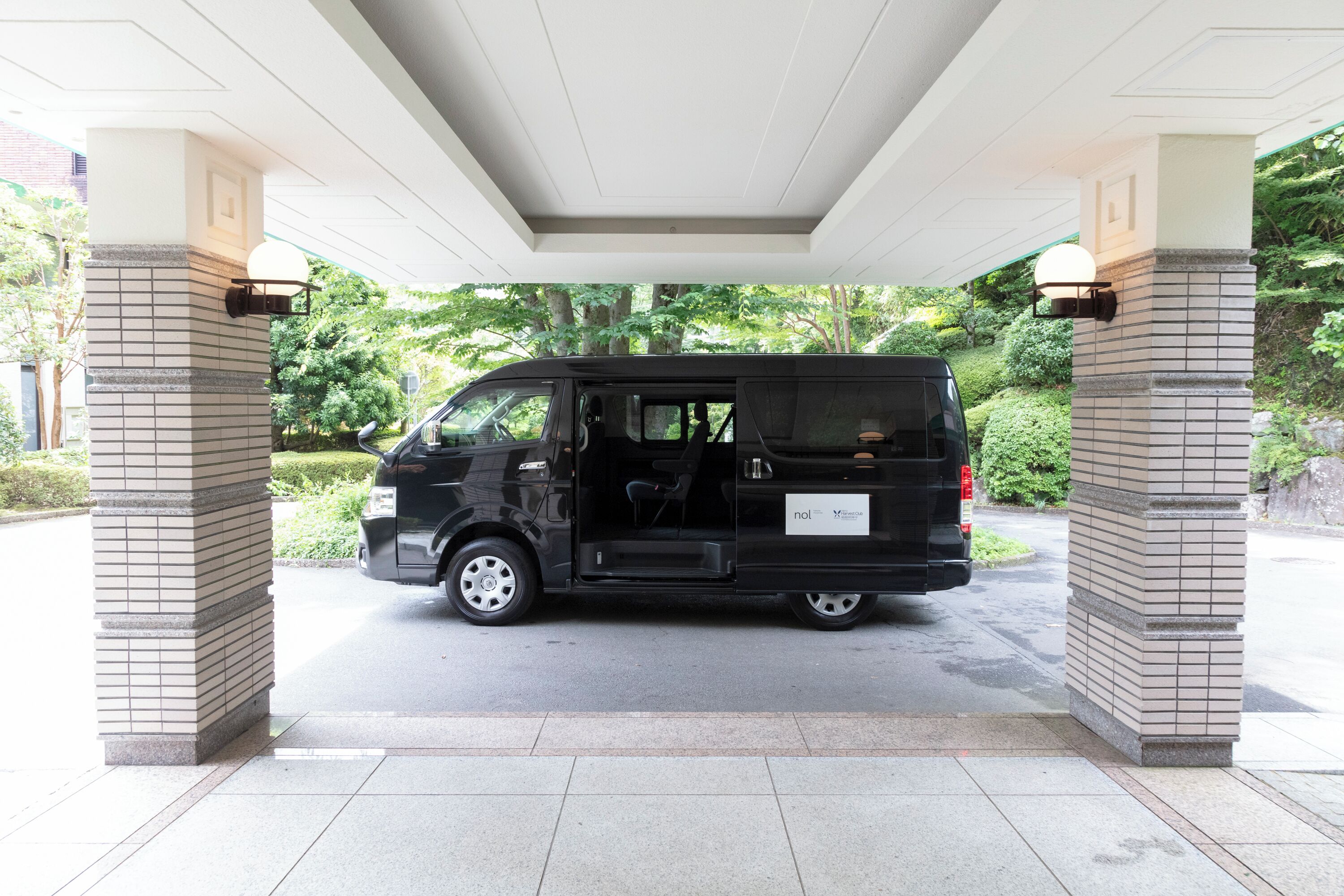 A black van parked under a covered area with brick pillars.