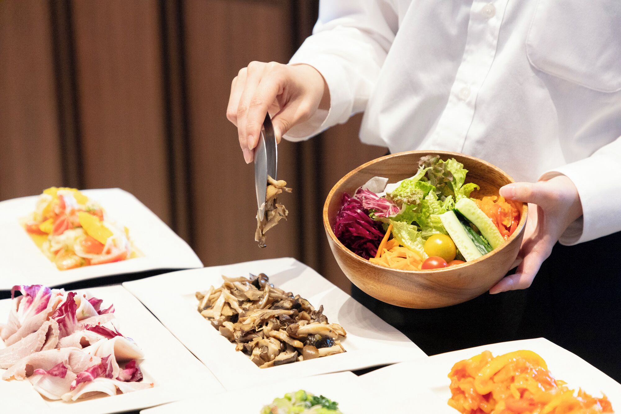 A person serving food from a wooden bowl to a plate.
