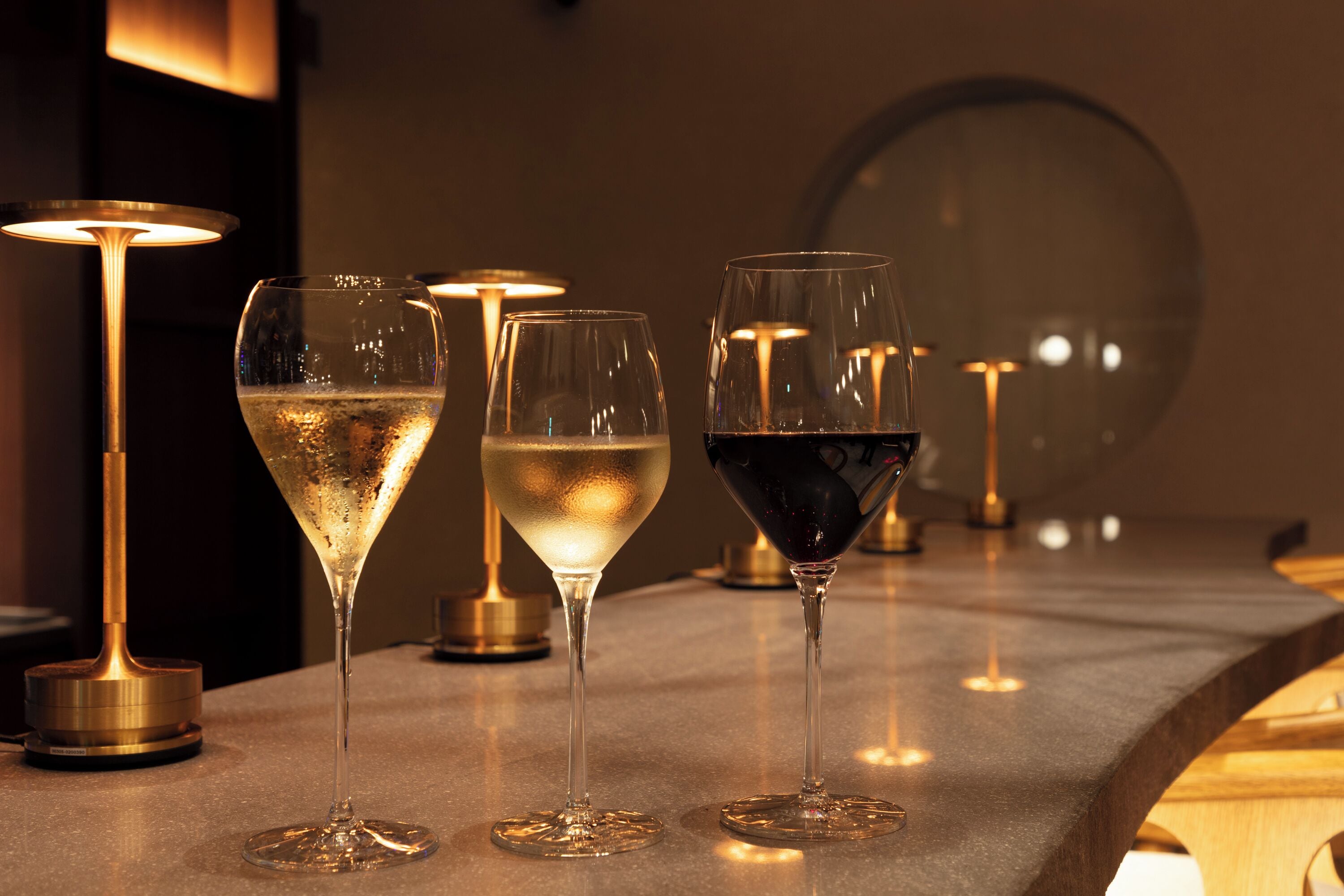 Three glasses of wine on a bar counter with a modern, minimalist design.