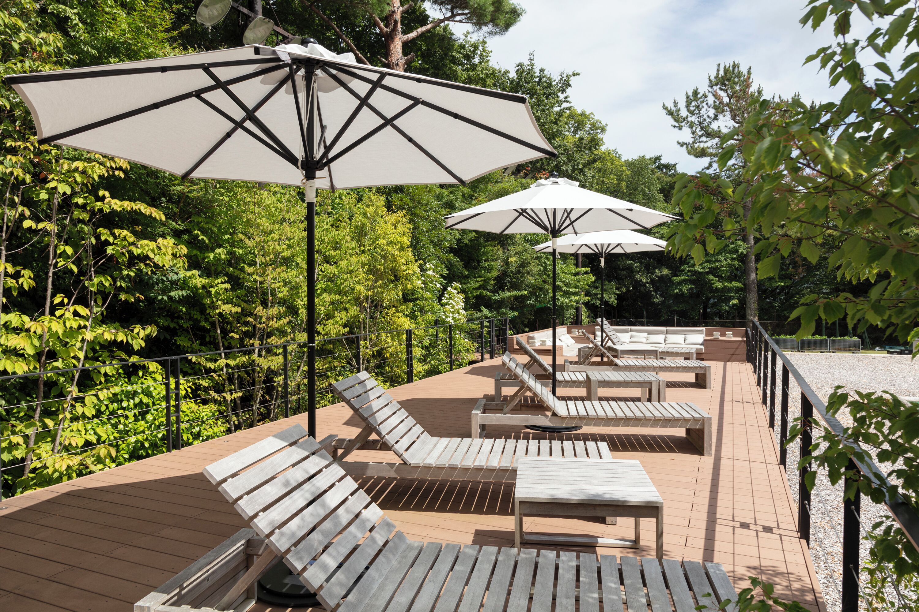 A deck with wooden lounge chairs and tables, surrounded by trees and a railing.
