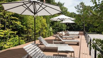 A deck with wooden lounge chairs and tables, surrounded by trees and a railing.