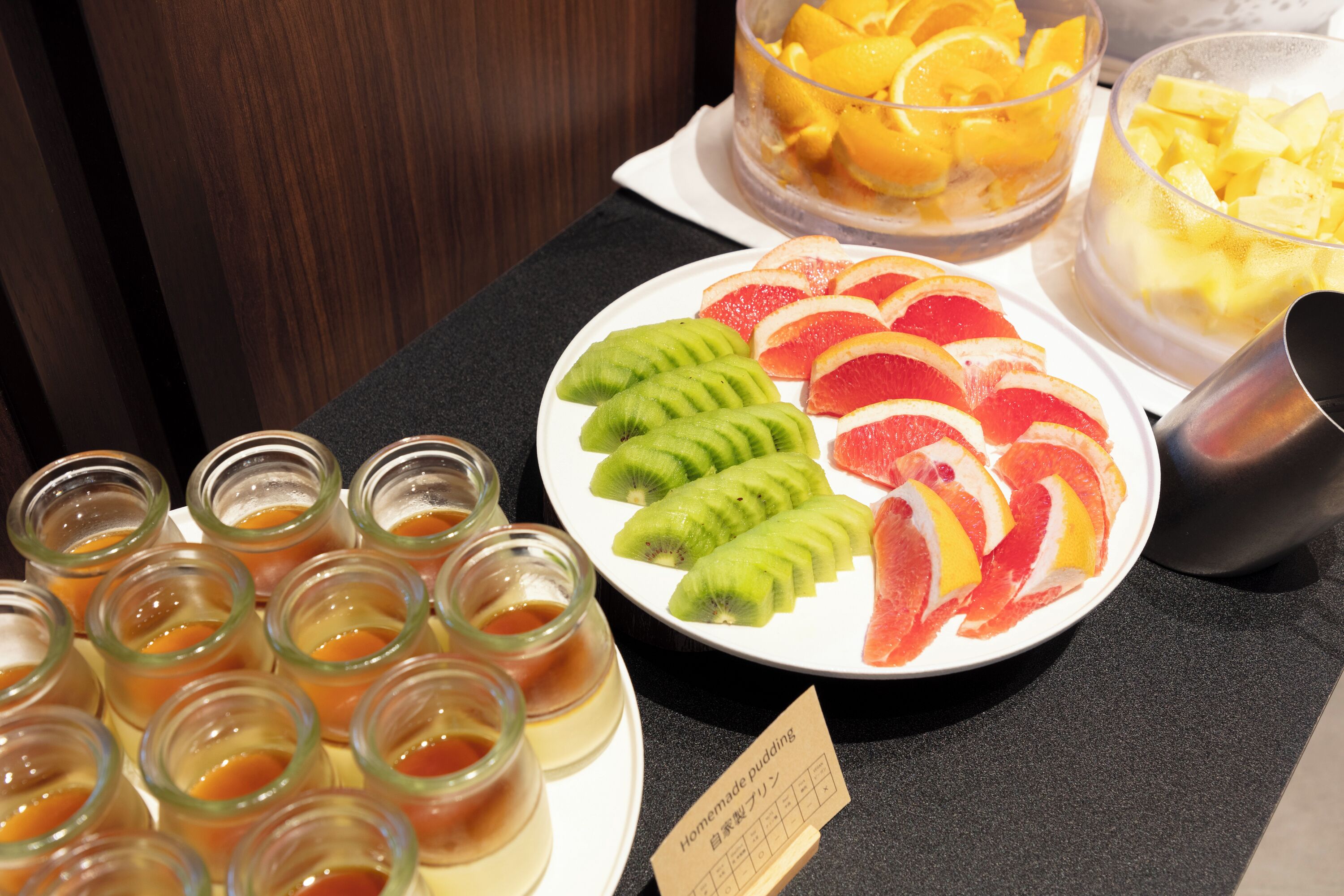 A fruit platter with kiwi, grapefruit, and orange slices, and several small jars of a condiment.