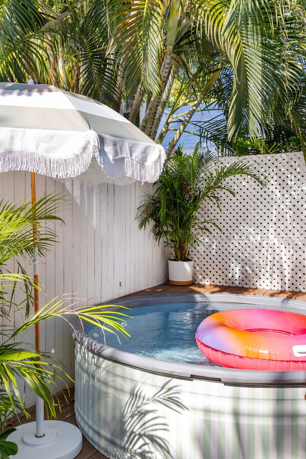 A hot tub with a striped cover, surrounded by potted plants and a white umbrella.