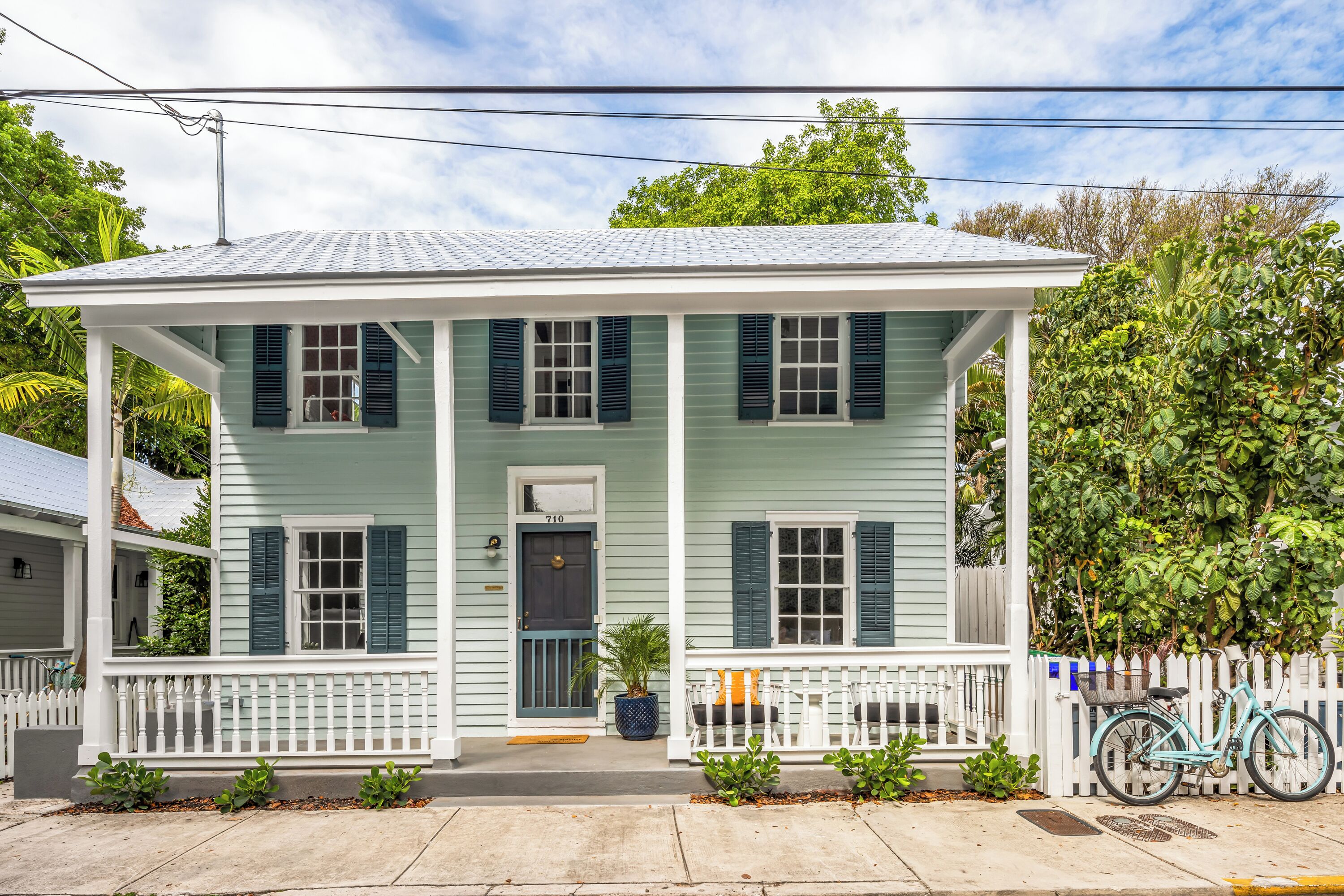 A two-story house with a porch, a bicycle, and a white picket fence.