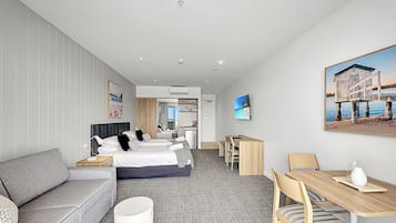 Ein Hotelzimmer mit Bett, einer Couch, einem Esstisch mit Stühlen, einem Fernseher und einem Bild an der Wand.