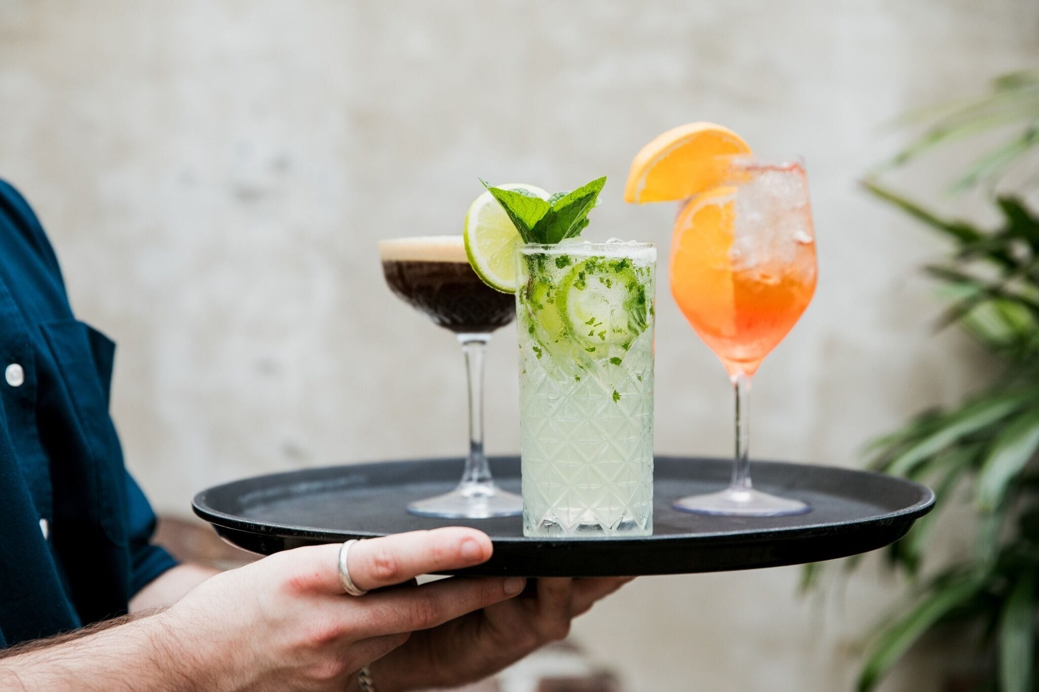 A person holding a tray with three different cocktails.