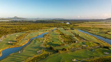 Ein Golfplatz mit mehreren Wasserhindernissen, Sandbunkern und einem Clubhaus in der Ferne.