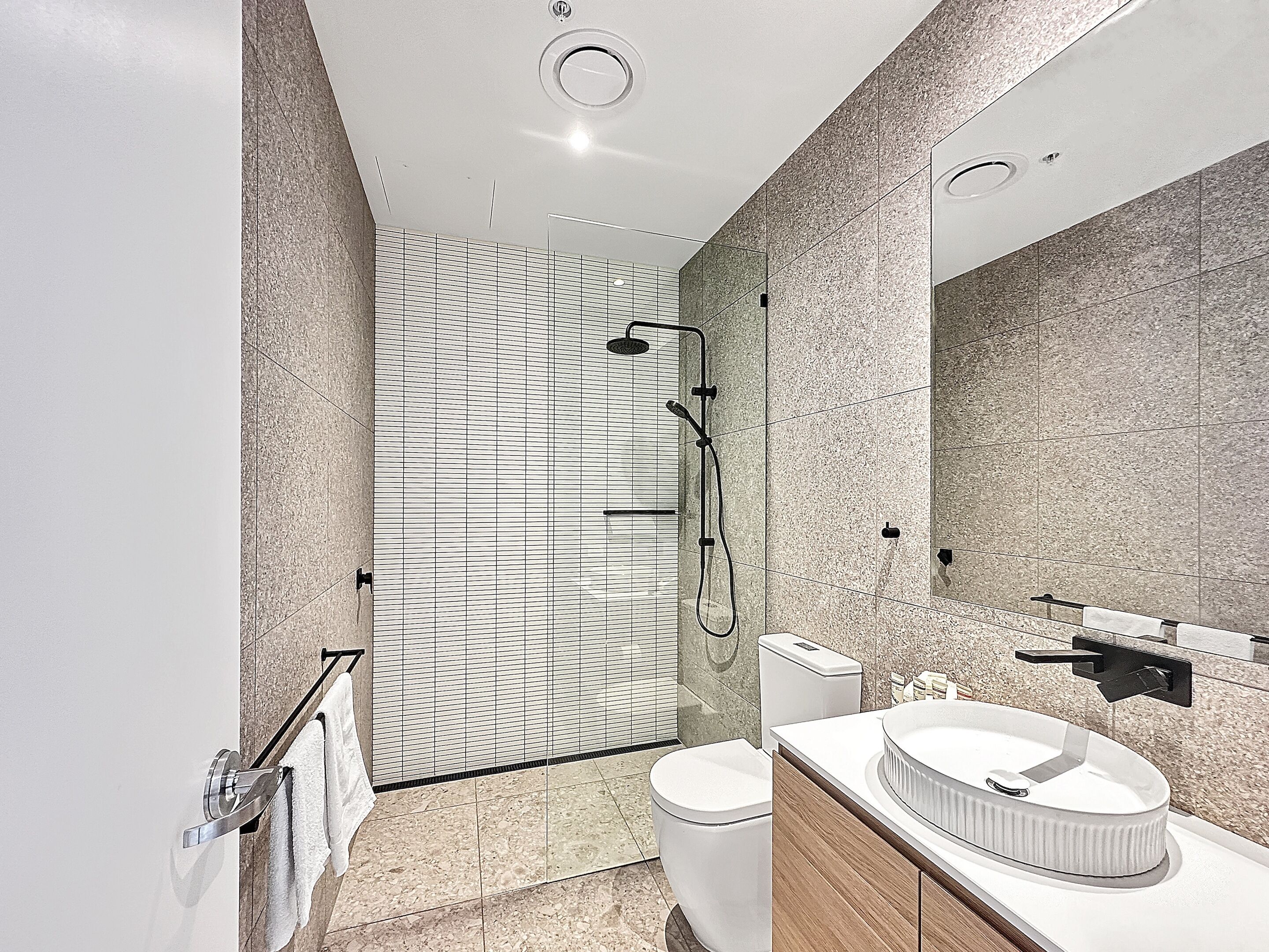 Un baño moderno con cabina de ducha de vidrio, inodoro blanco y tocador con lavabo redondo.