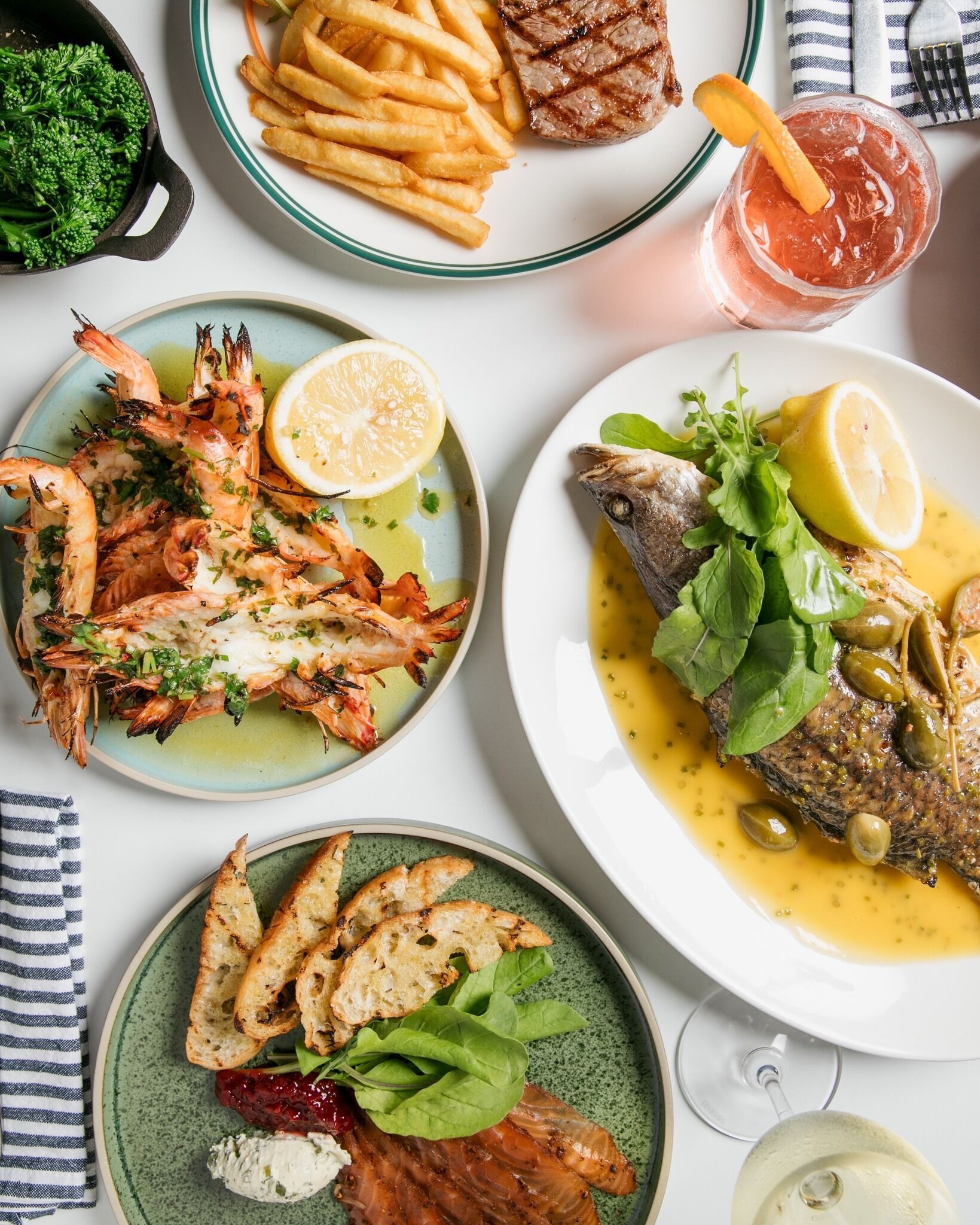 A table with various dishes including grilled steak, shrimp, fish, and bread.