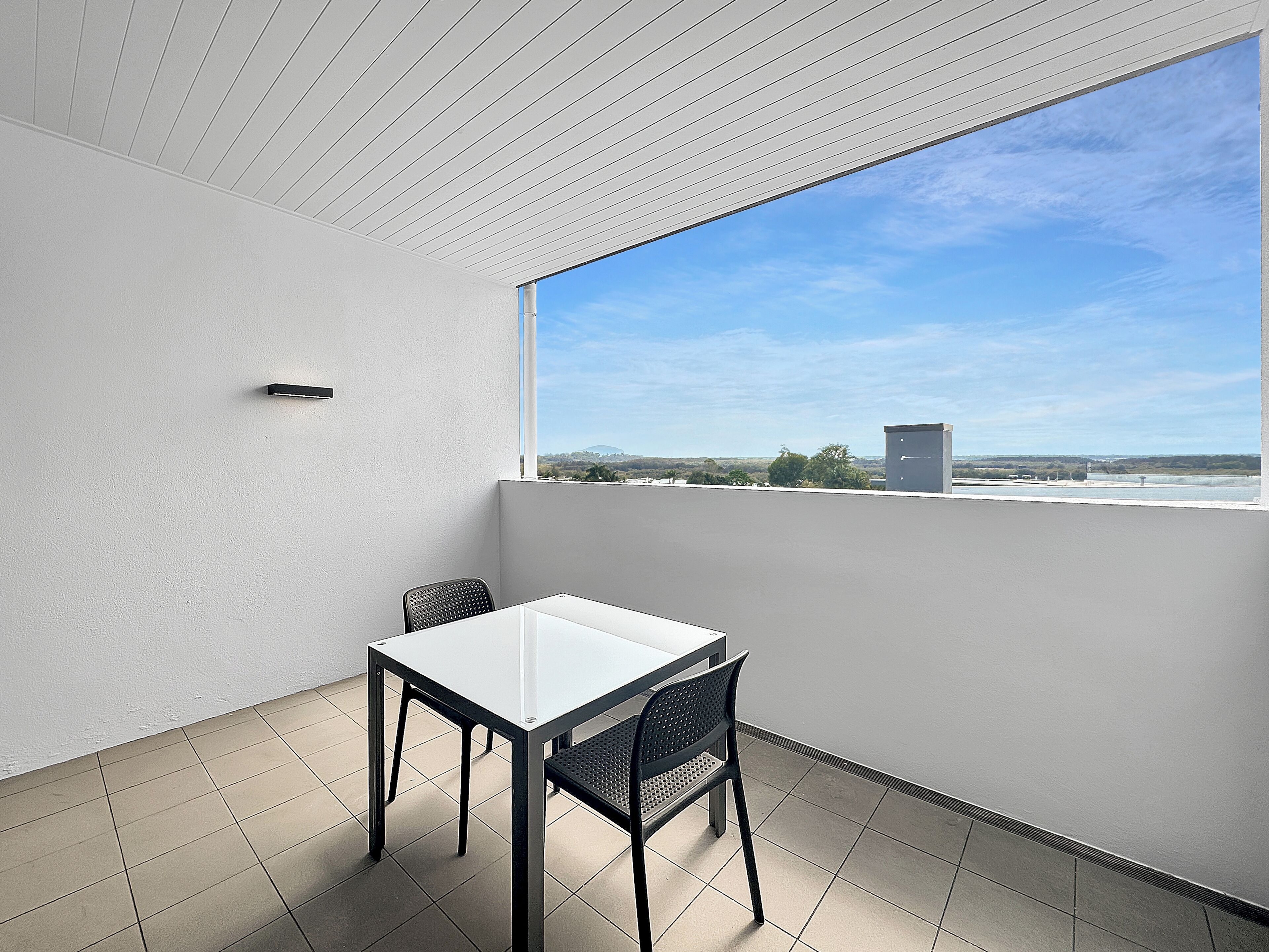A balcony with a table and chair, a view of the sky, and a distant landscape.
