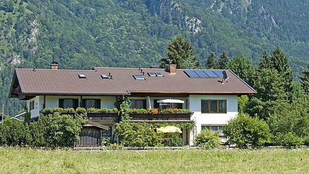 Una casa de dos pisos con techo inclinado, paneles solares y un jardín delantero.
