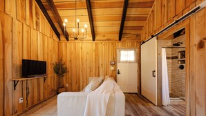 Une pièce chaleureuse avec des murs en bois, un canapé blanc, un téléviseur posé sur une étagère et une porte coulissante donnant sur une autre pièce.