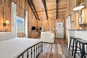 A wooden cabin interior with a bed, a sofa, a desk, and a television. - Family-Friendly Creekside Cabin, Space to Roam + Play (Smithville)