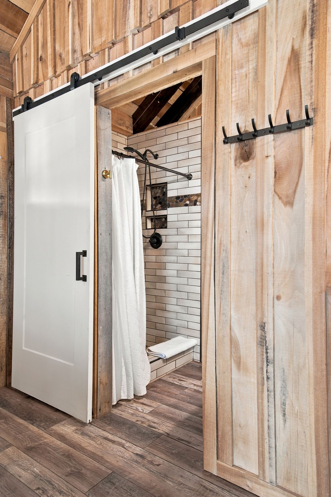 Un baño rústico con pared de madera, una puerta blanca y un perchero.