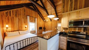 L’intérieur d’un chalet en bois comprend un lit, une cuisine équipée d’appareils électroménagers modernes et une grande fenêtre.