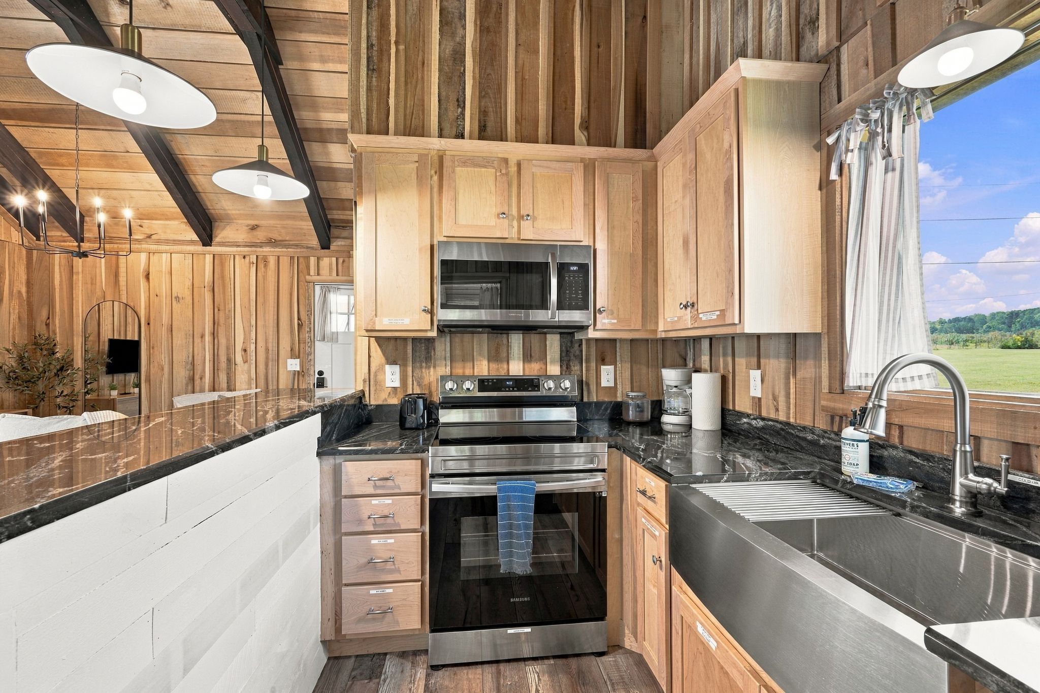 A modern kitchen with wooden cabinetry, stainless steel appliances, and a large window offering a view of the outdoors.