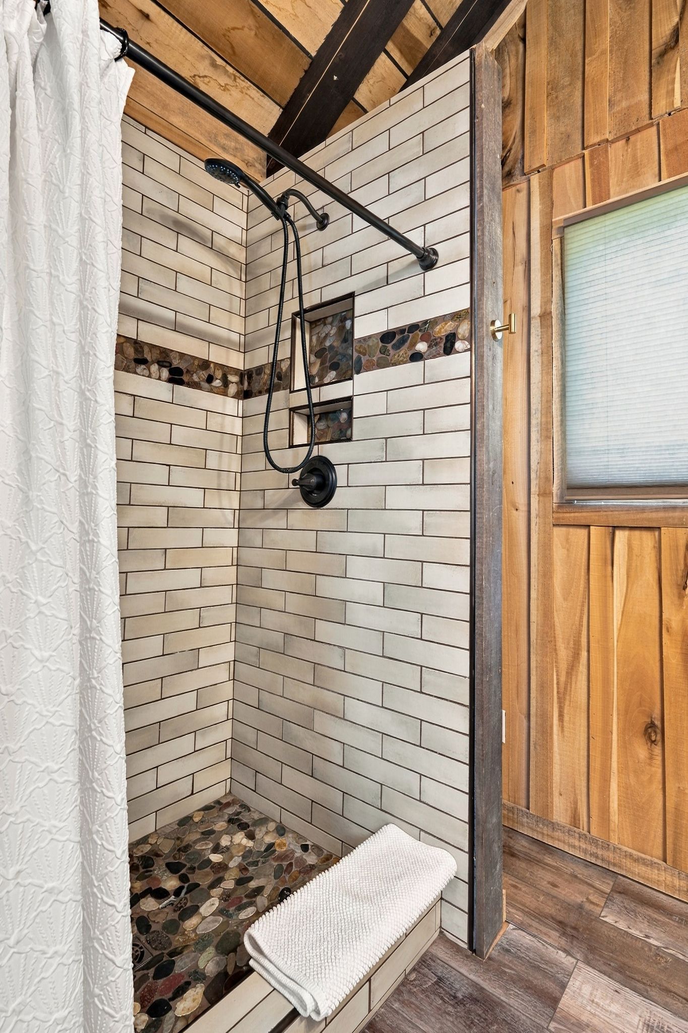 A shower with a stone mosaic wall, a bench, and a wooden door.