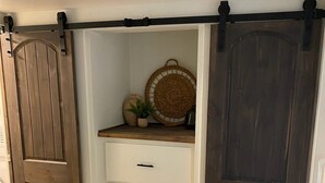 Ein Schlafzimmer mit einem Bett, einem Schminktisch, einer Schiebetür im Bauernhausstil und einem kleinen Regal mit Dekorationen.