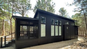 Eine moderne Holzhütte mit überdachter Veranda, großen Fenstern und einem Wald im Hintergrund.