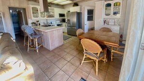 A spacious kitchen with a central island, a dining area with wicker chairs, and a ceiling fan.