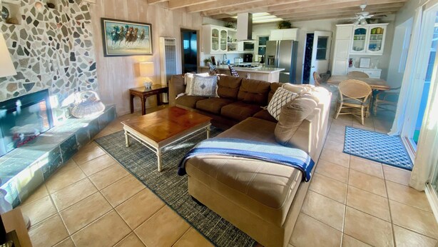 A living room with a stone wall, a fireplace, a sofa, a coffee table, and a kitchen in the background.
