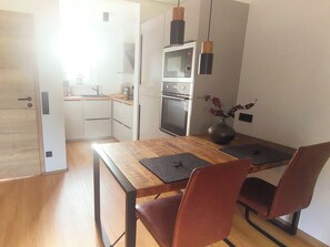 Une cuisine compacte dotée d’un four et d’un micro-ondes encastrés, d’un plancher en bois et d’un coin repas avec une table et des chaises.