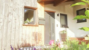 A wooden house with a small window, a door, and a porch area with plants and flowers. - Studio apartment for 2 persons with terrace, 34 m² (Inzell)