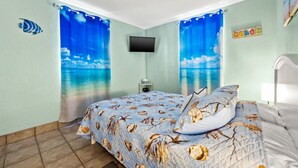 Une chambre à coucher avec un lit, un téléviseur et des rideaux représentant une scène de plage.