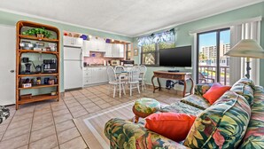 Un salon comprenant un canapé, une table basse et un téléviseur. Il y a également un coin cuisine avec des placards et une table à manger avec des chaises.