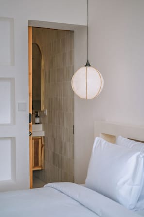 Habitación de hotel con una cama, una lámpara colgante y una puerta de madera que da a un baño.