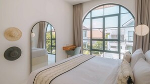 Une chambre à coucher avec un grand lit, un miroir et une vue sur l’extérieur grâce à une grande fenêtre.