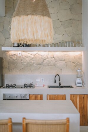 A kitchen with a stone backsplash, wooden cabinets, a white countertop, a gas stove, a sink, and a hanging light fixture.