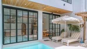 Un espace piscine intérieur moderne, doté de murs en verre, de chaises longues et d’un plafond avec des lambris en bois.