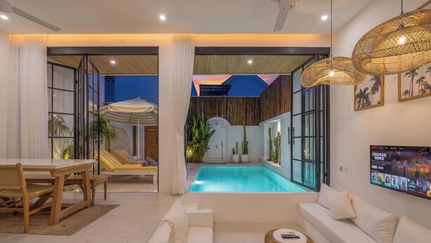 Un salon moderne avec une piscine, des canapés blancs, un coin repas et un téléviseur diffusant un film.