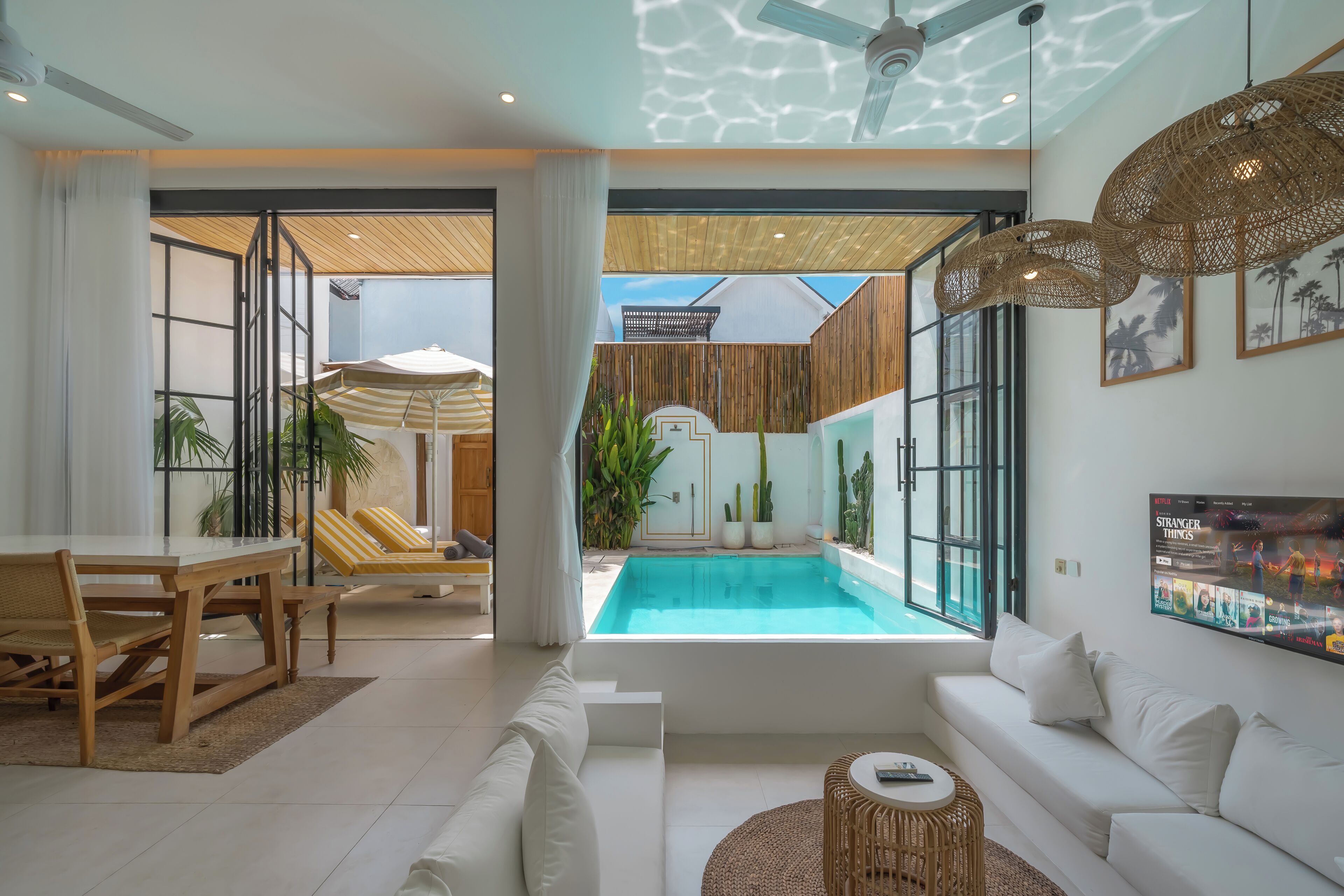 Ein modernes Wohnzimmer mit Blick auf einen Pool, weiße Möbel und ein Deckenventilator.
