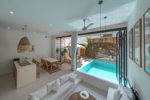 A modern living room with a pool view, a dining area, and a ceiling fan.