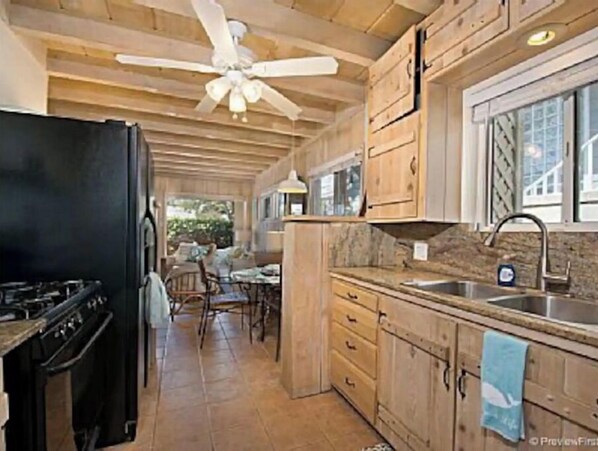 A kitchen with wooden cabinets, a black refrigerator, a stove, and a ceiling fan. - Surfside Cottage - 200 ft from the Sand (Del Mar)