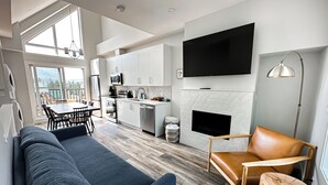 Een moderne woonkamer met een bank, een eettafel en een keuken met witte kasten en een flatscreen televisie.