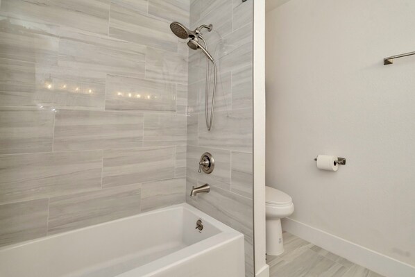 Un baño moderno con una bañera blanca, ducha con cabezal de mano y un inodoro.