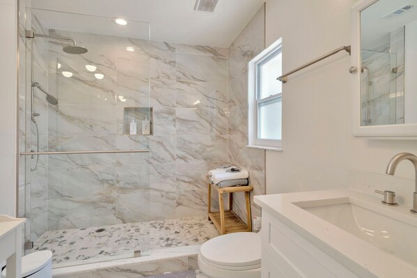A modern bathroom with a glass-enclosed shower, a white sink, and a marble-tiled wall. - The Bay Beach House: Boat/Jetskis (Tampa)