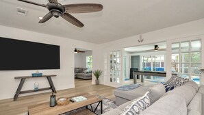 Ein geräumiges Wohnzimmer mit großem Flachbildfernseher, Deckenventilator und Couchtisch aus Holz.