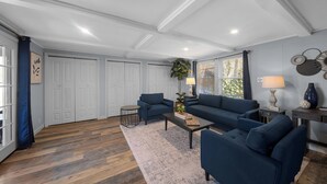 Un salon moderne avec un canapé bleu, une table basse et un tapis. On y trouve des portes blanches et une fenêtre avec des rideaux.