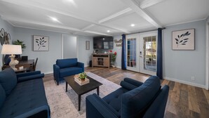 Un salon spacieux avec un grand canapé, une table basse et un coin cuisine visible à travers une porte vitrée.