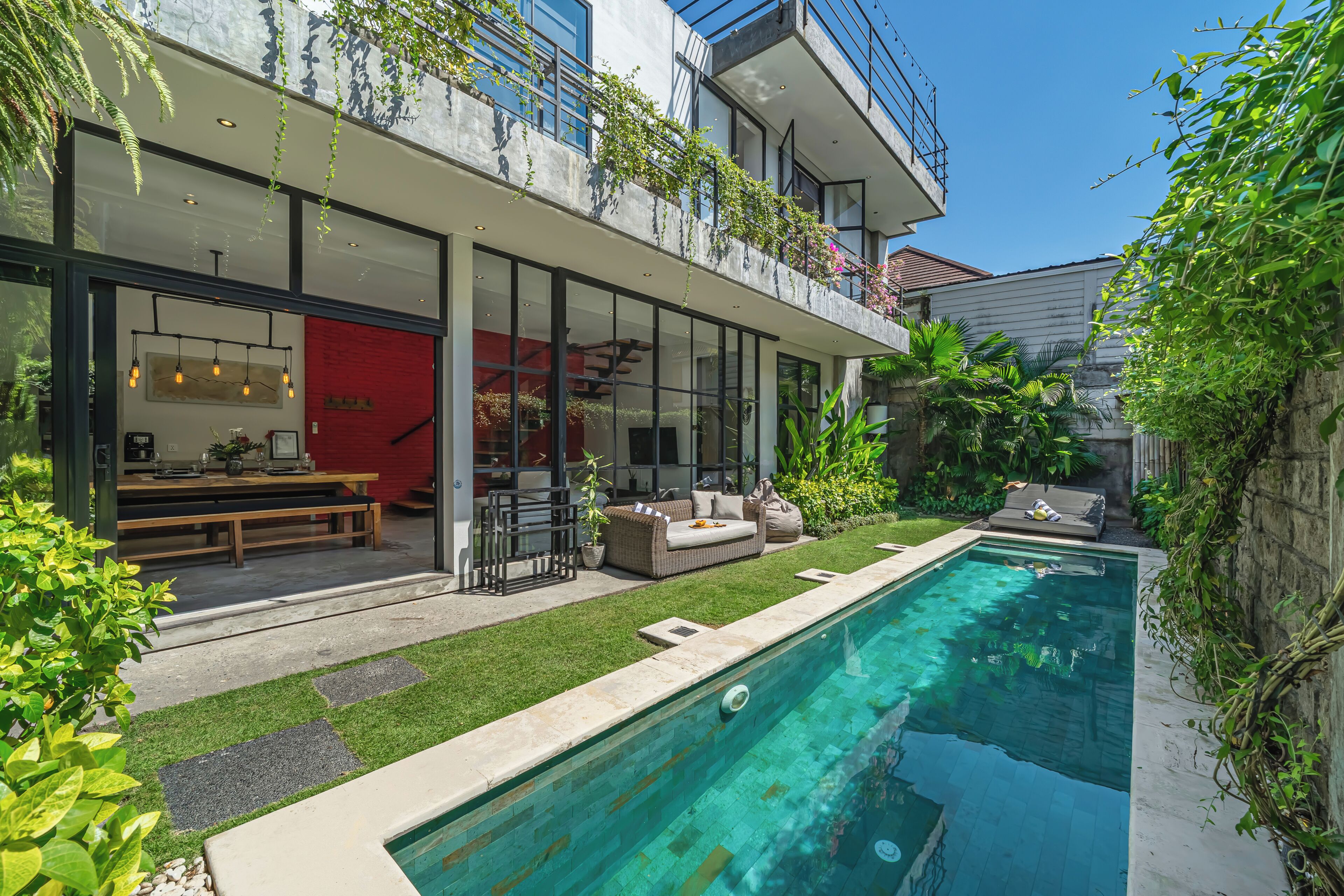 Une maison moderne dotée d’une piscine, d’un espace salon extérieur et d’un mur rouge.