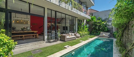 Une maison moderne dotée d’une piscine, d’un espace salon extérieur et d’un mur rouge.