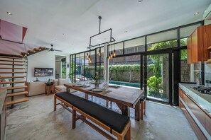 A modern kitchen with a dining area, large windows, and a pool view. - Villa Jungalow 2BR Pool Villa Near Beach Café del Mar & Padel (Canggu)