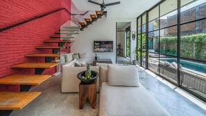 A modern interior with a staircase, a sofa, a coffee table, and a view of a swimming pool. - Villa Jungalow 2BR Pool Villa Near Beach Café del Mar & Padel (Canggu)