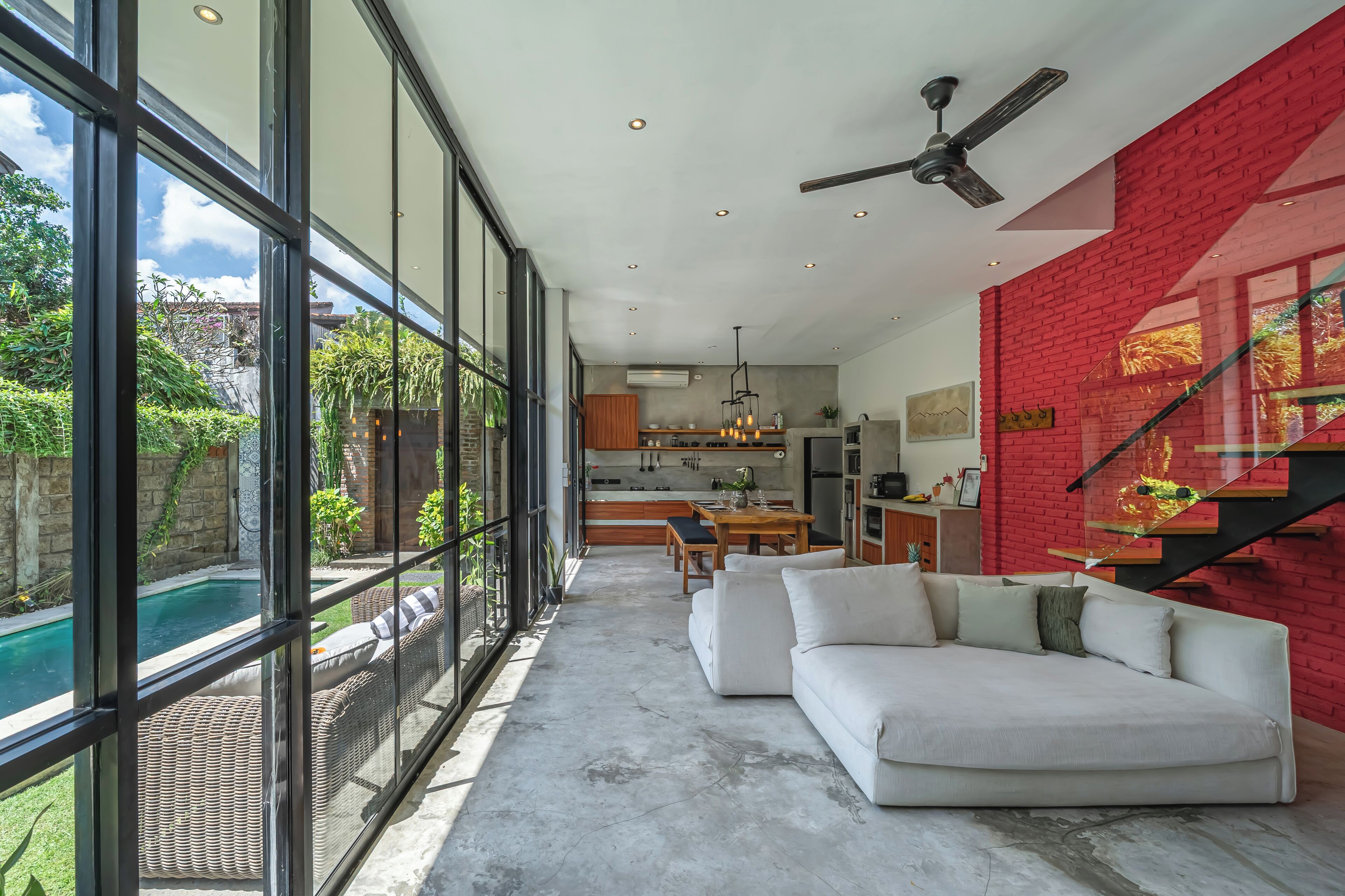 A modern living space with a large glass wall, a red brick wall, a white sofa, and a dining area.