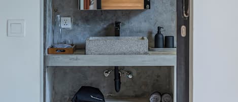 A bathroom with a concrete wall, wooden cabinet, and a sink with a soap dispenser.